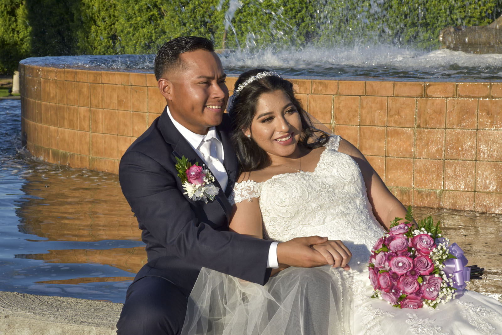 Pareja recién casada en Mesa, Arizona, posando junto a una fuente con flores rosadas.